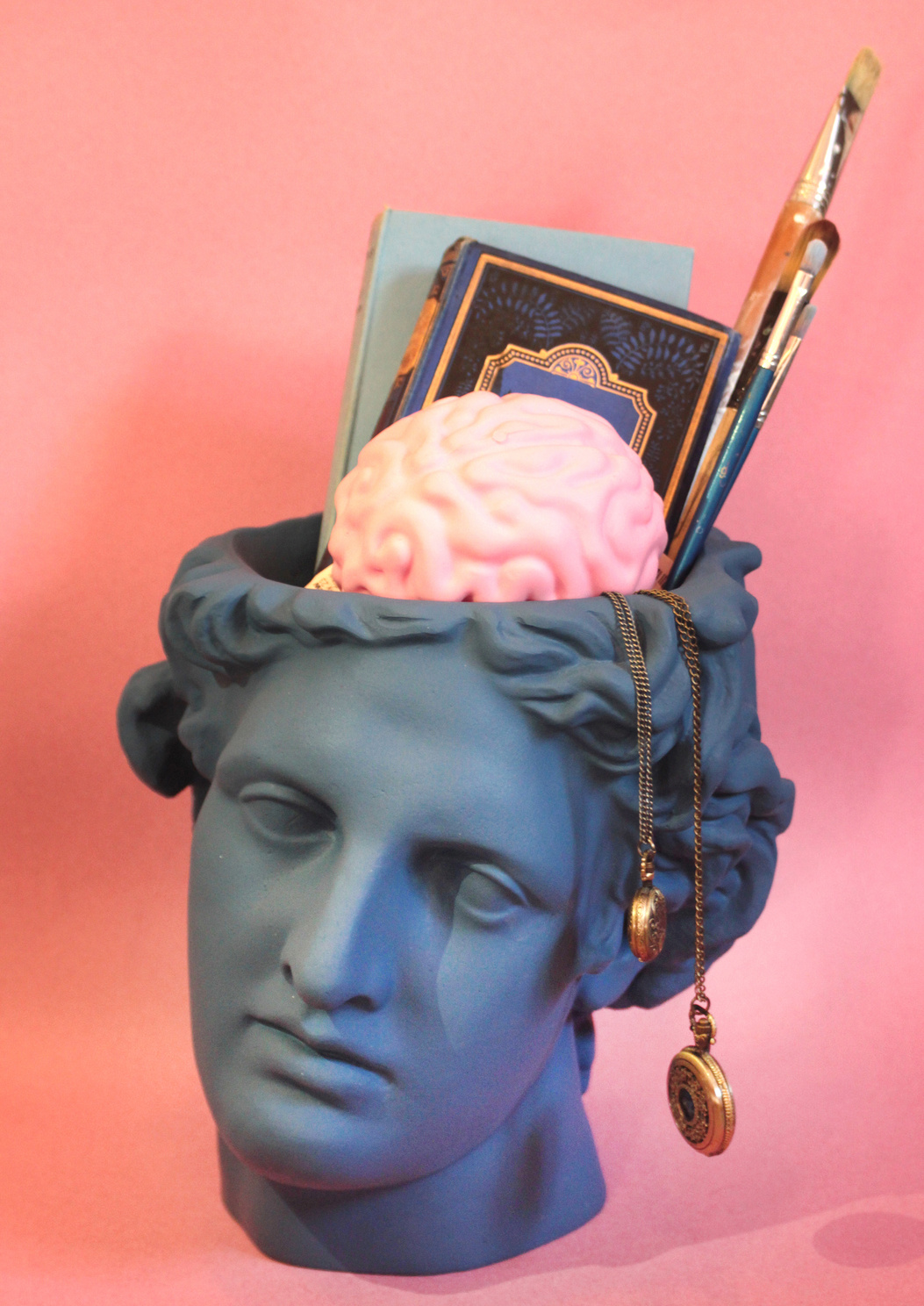 A blue statue of a head with books, paintbrushes, watches and a pink brain in it